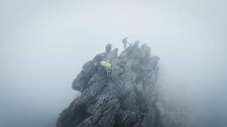 Drei Kletterer klettern einen felsigen Grat im Nebel hoch.