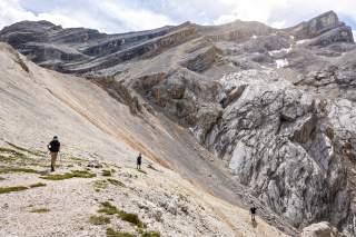 Drei Männer beim Abstieg auf einem schottrigen Weg im kargen Hochgebirge.
