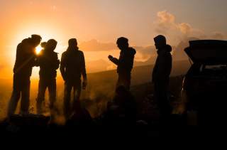 Gruppe von Menschen steht bei Auto im Sonnenuntergang