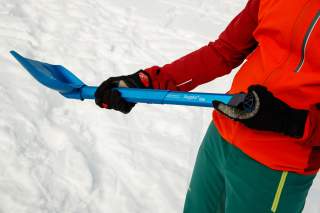 Person im Schnee mit Lawinenschaufel in der Hand