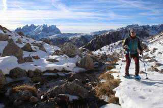 Person wandert mit Schneeschuhen an Bergbach entlang