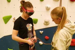 Eine junge Frau mit einer großen undurchsichtigen Brille knotet sich ins Kletterseil ein.