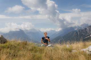 Frau macht Atemübungen auf Bergwiese